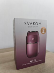 Caja del estimulador Klitty de SVAKOM sobre superficie textil clara